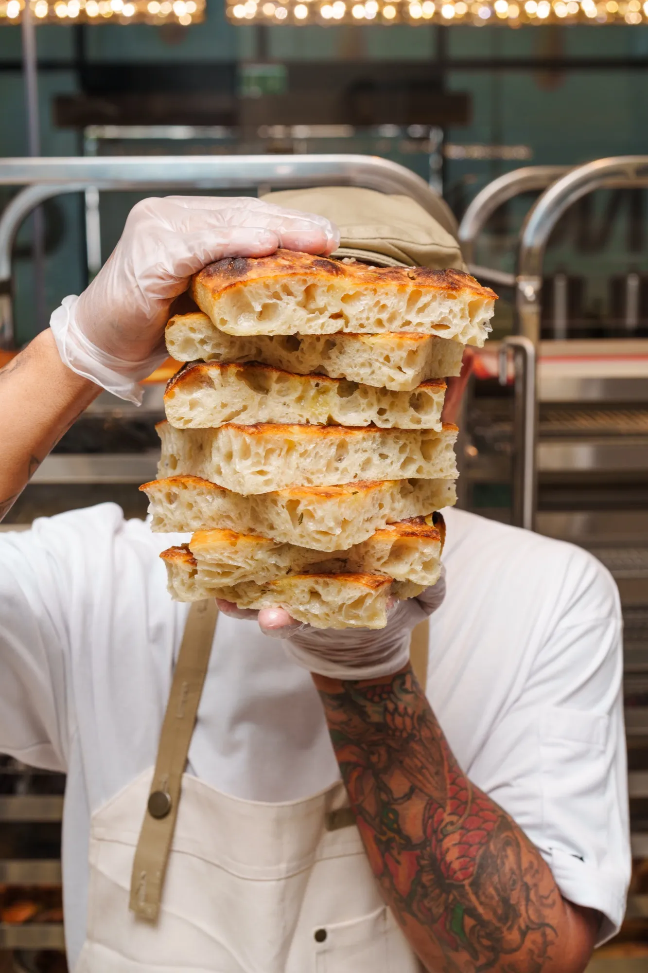 A baker holding a stack of fresh focaccia in the kitchen