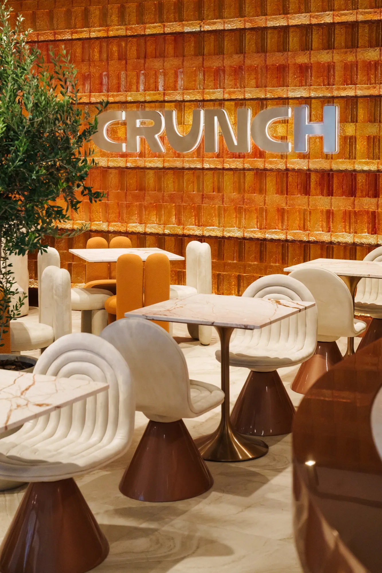 The CRUNCH dining room — amber glass wall, marble tables and curved cream chairs
